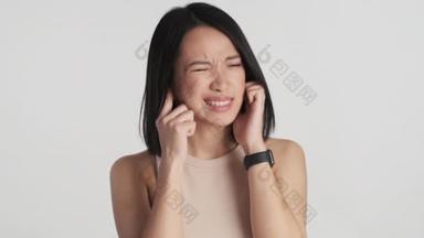 年轻的亚洲女人用手指捂住耳朵，因为它在白色背景上的声音太大了。我不想听